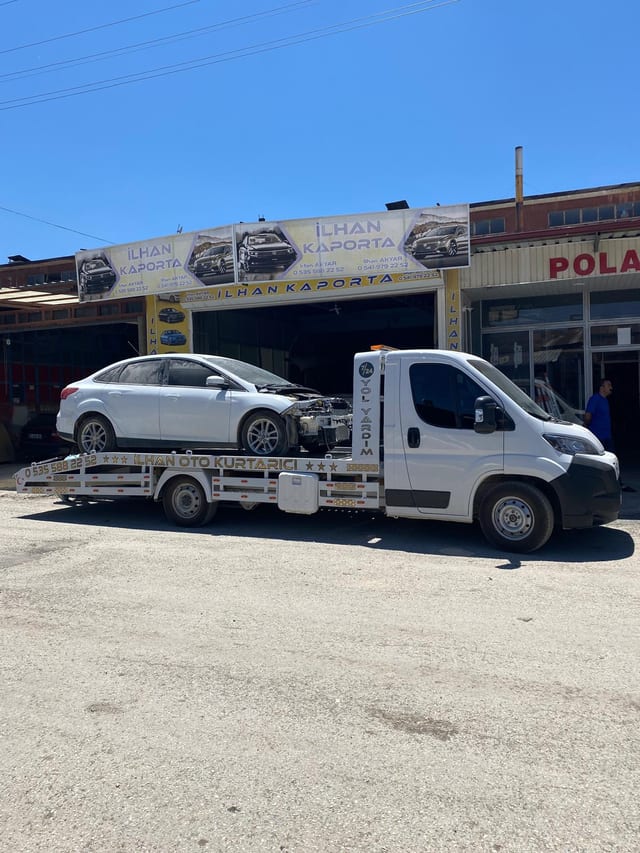 İş yeri önünde platformunda gümüş otomobil bulunan çekici