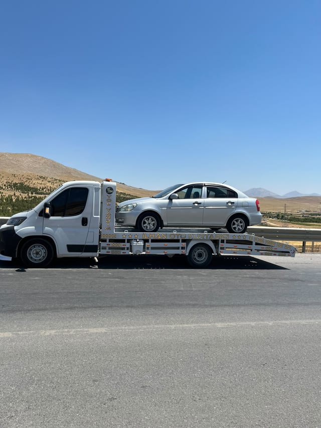 Yol üzerinde platformunda gümüş sedan bulunan çekicinin yandan görünümü